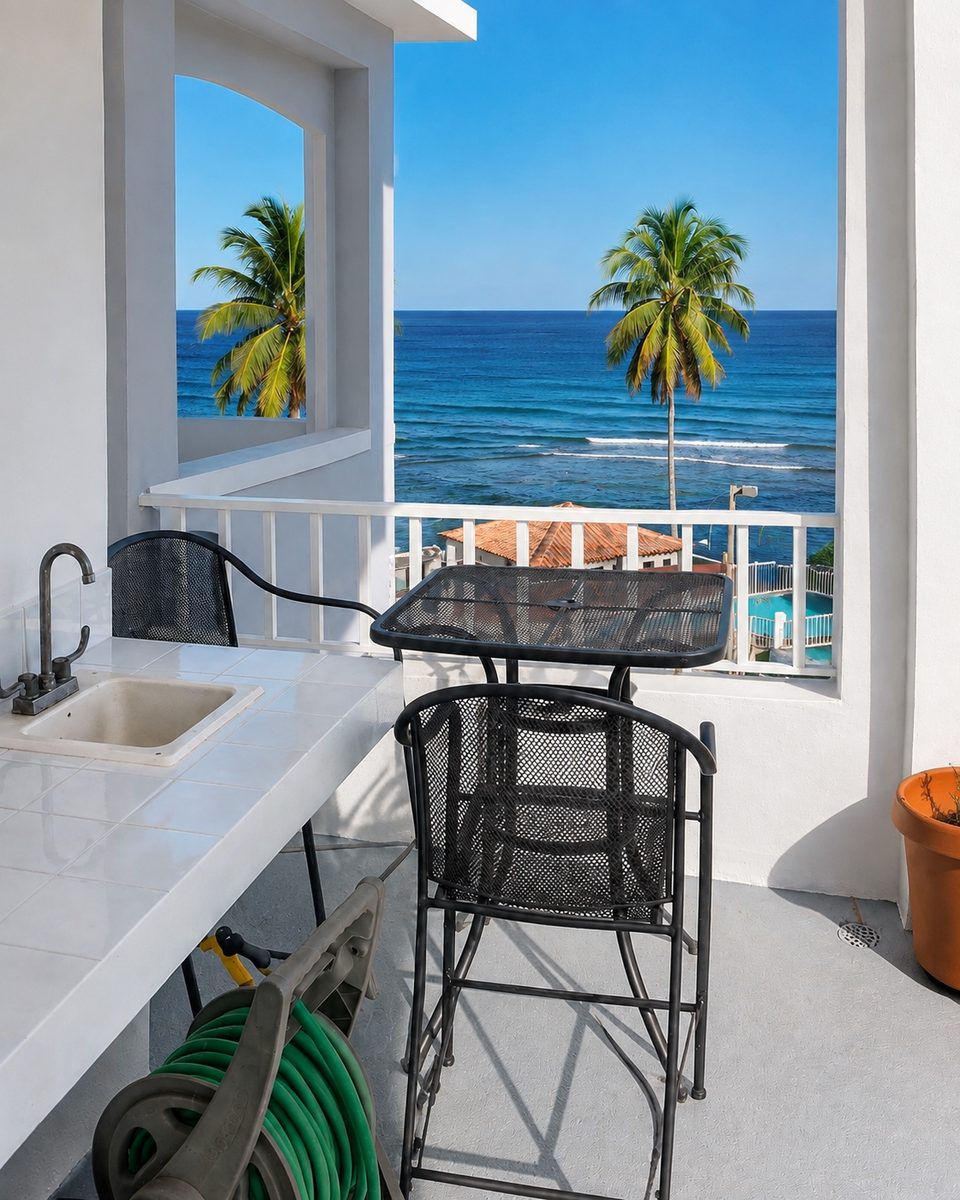 Bistro table and stools beside the balcony's outdoor sink, the ocean through the palms