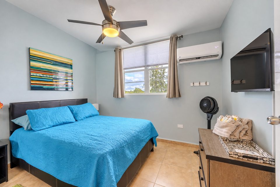 Bedroom two from the door: the blue bed under the window, striped art on the wall, the TV to the right
