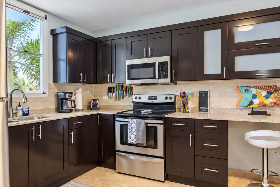 The L-shaped kitchen: stainless electric range and microwave, the sink under a window of palms, coffee maker on the counter