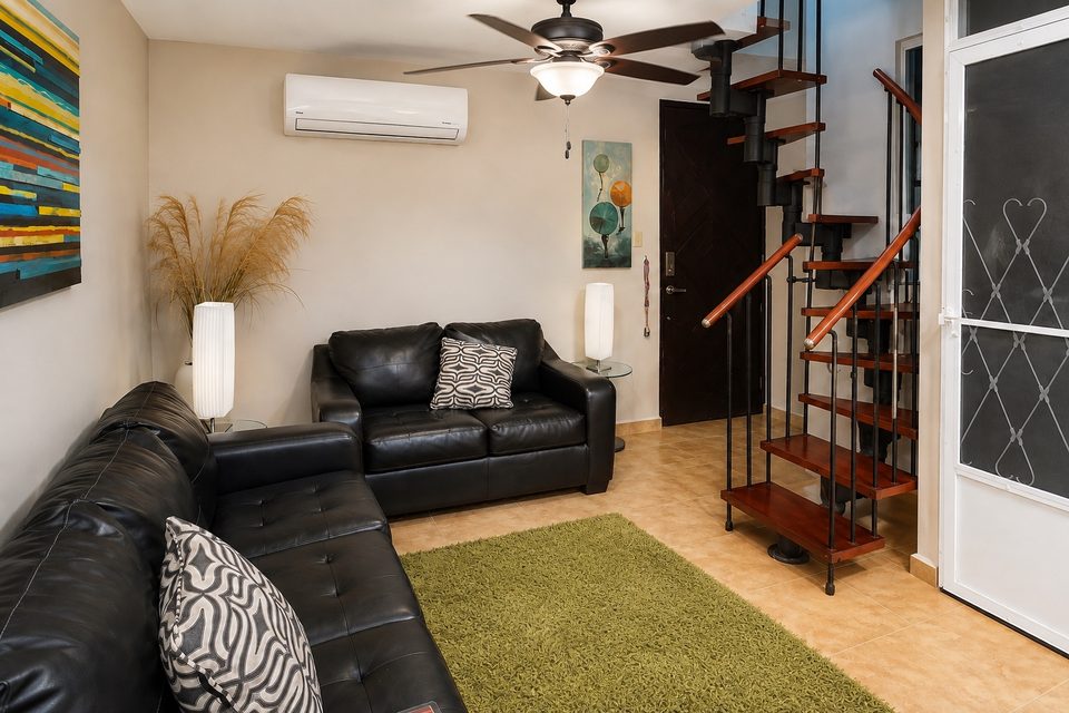 The living room: black leather sofa and loveseat, a green rug, the red-and-black spiral stair to the loft, a ceiling fan and the front door
