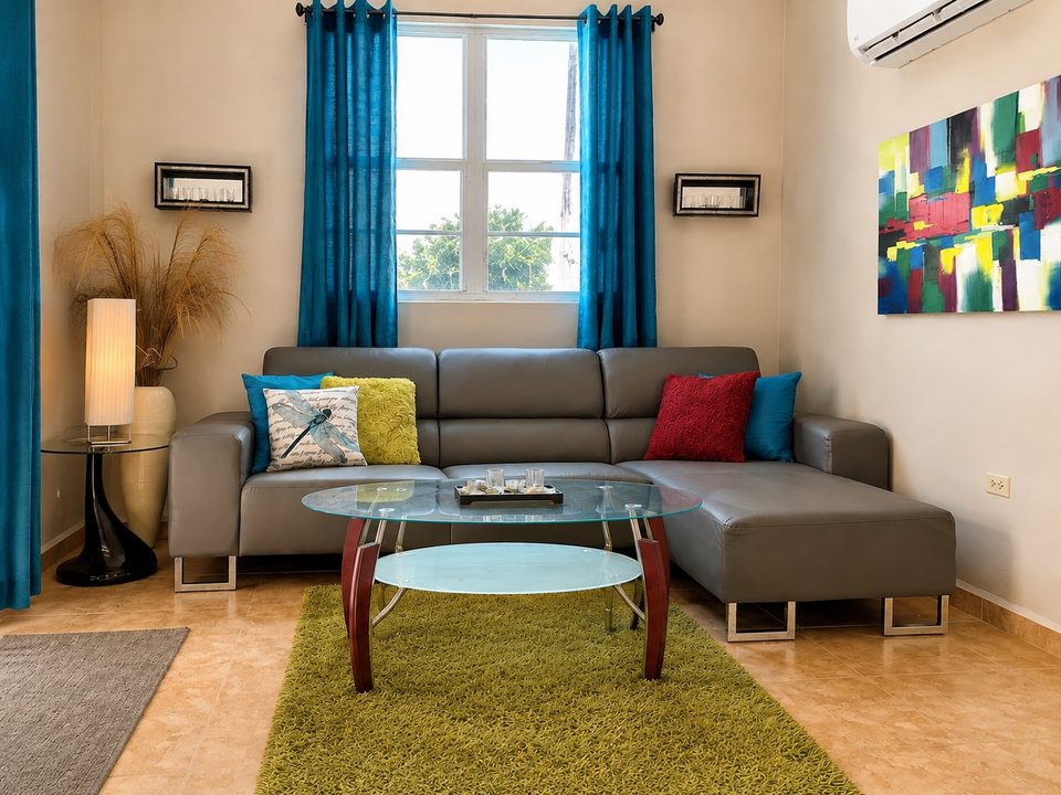 The living room seating area: grey sectional, glass coffee table, green rug, ductless air conditioning and bright windows