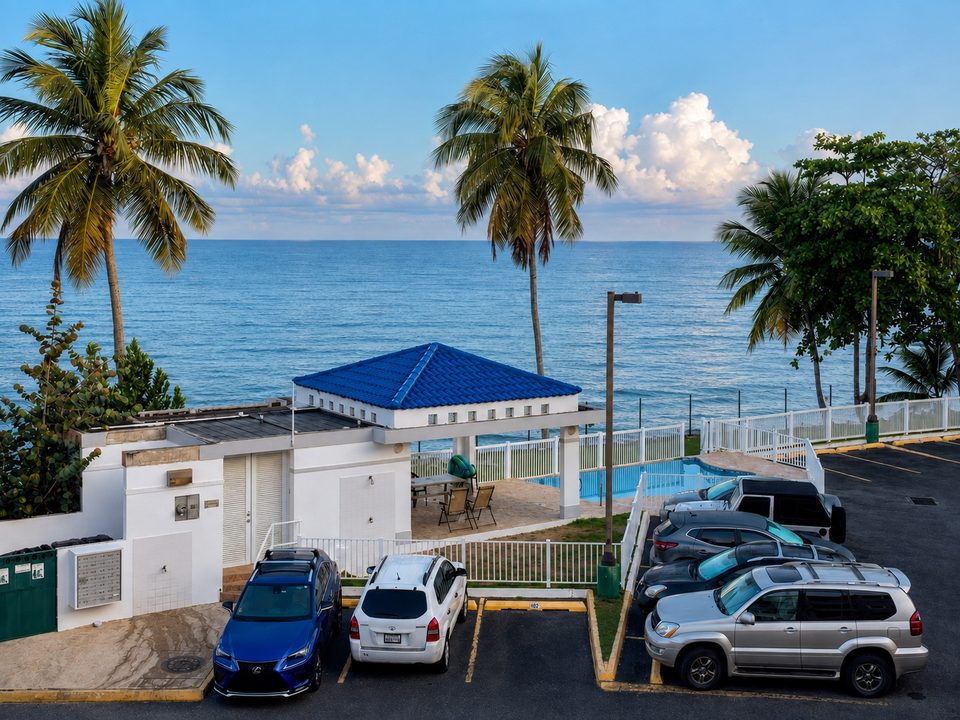 From the balcony: palms, the pool pavilion's blue roof, the parking court and the ocean
