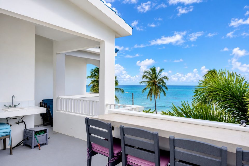 The rooftop counter and stools beside the outdoor sink, white railing, palms and the Atlantic straight ahead