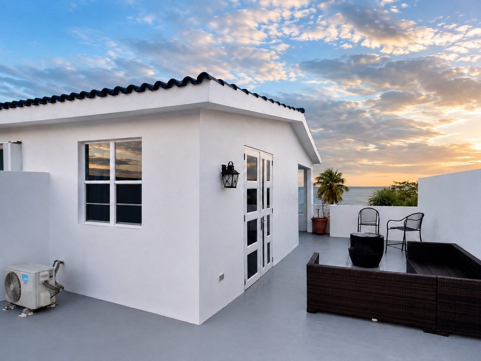 The rooftop terrace under a wide sky: white walls, the rooftop room and the ocean to one side